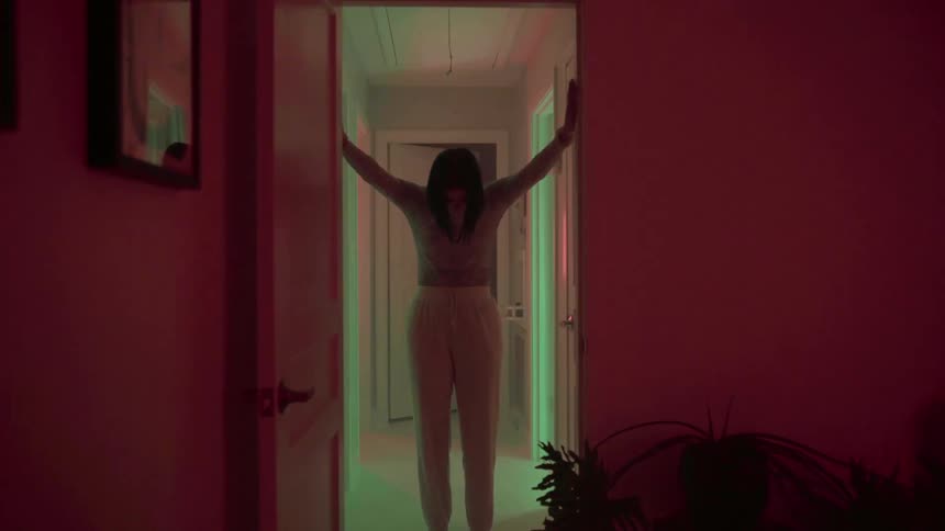 Woman leans in doorway while colored lights tint the hallway