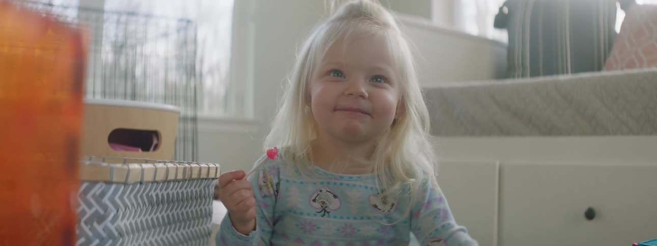 A little girls laughs as she eats a lollipop