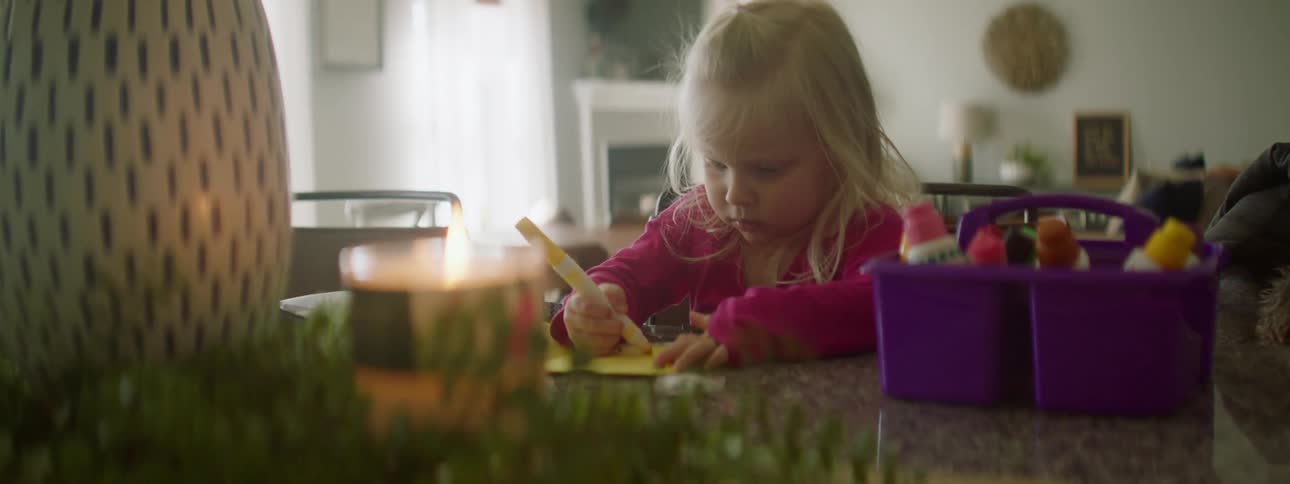 Little blonde girl sitting at kitchen island drawing on yellow paper