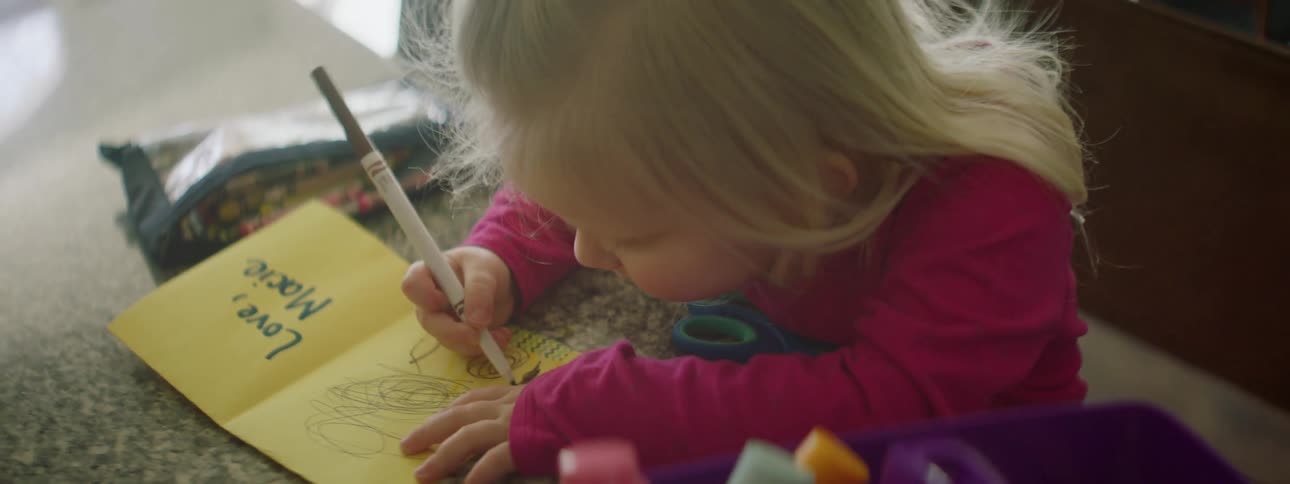 A young girl sits at a table and colors with a marker
