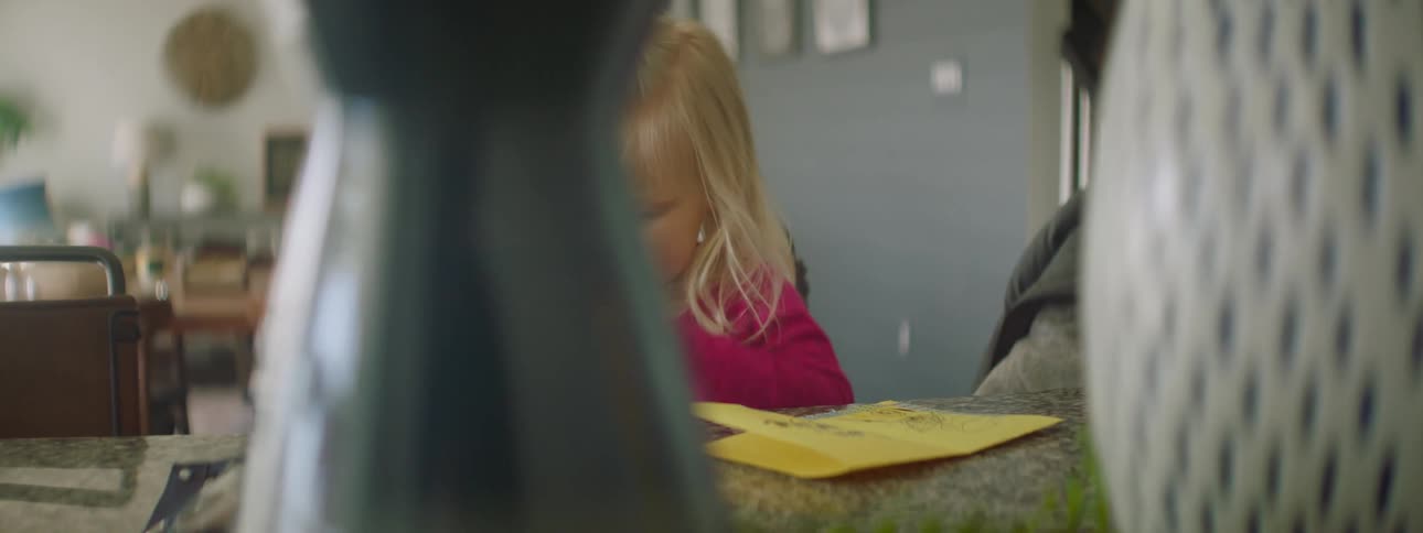 A little girls sits at a table and does crafts as her parent sits beside her
