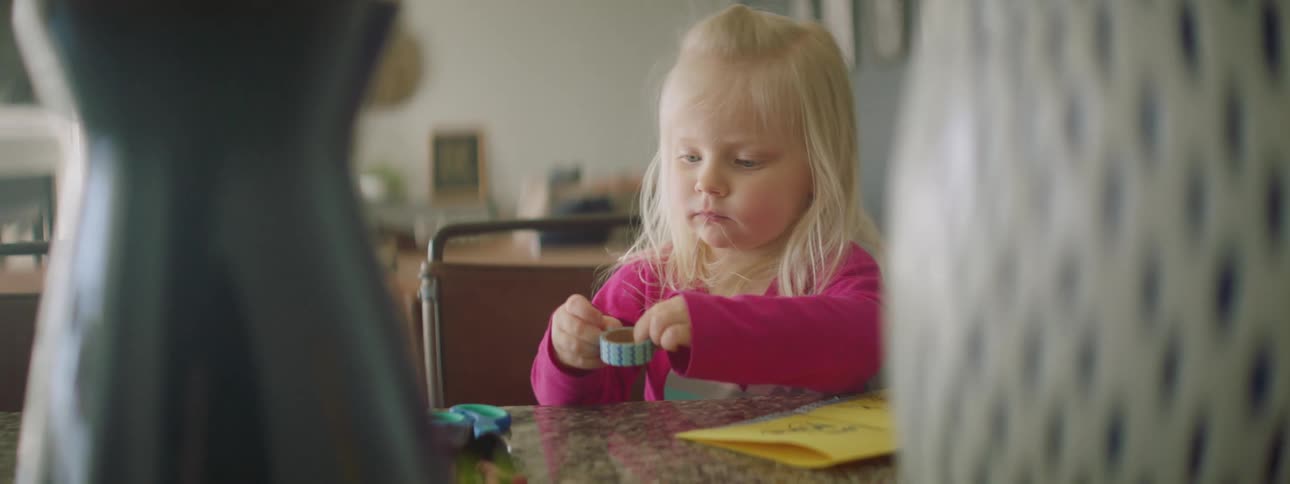 A little girl sitting at a table peeling tape