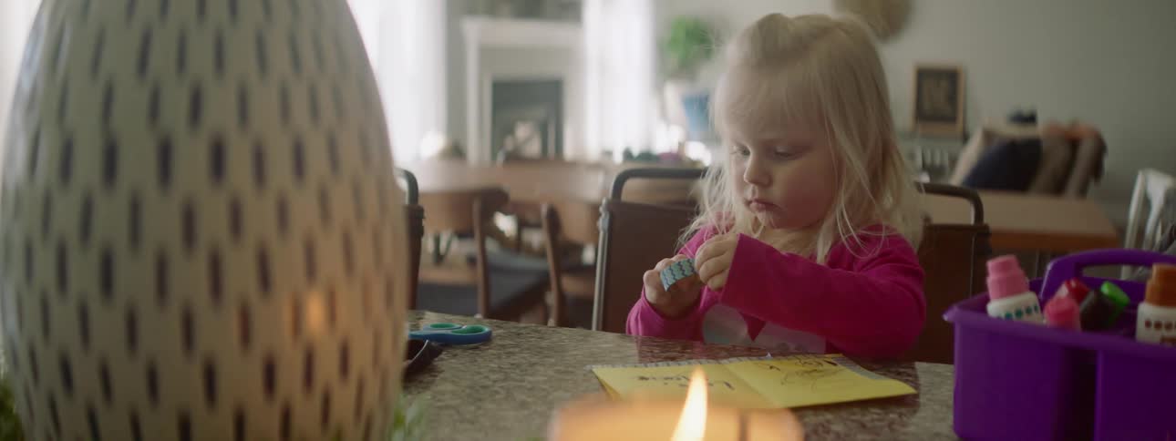 A white child sits at a table and puts a piece of tape on some paper
