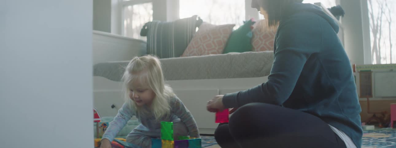 A teenage girl sits on the floor and plays with a younger girl