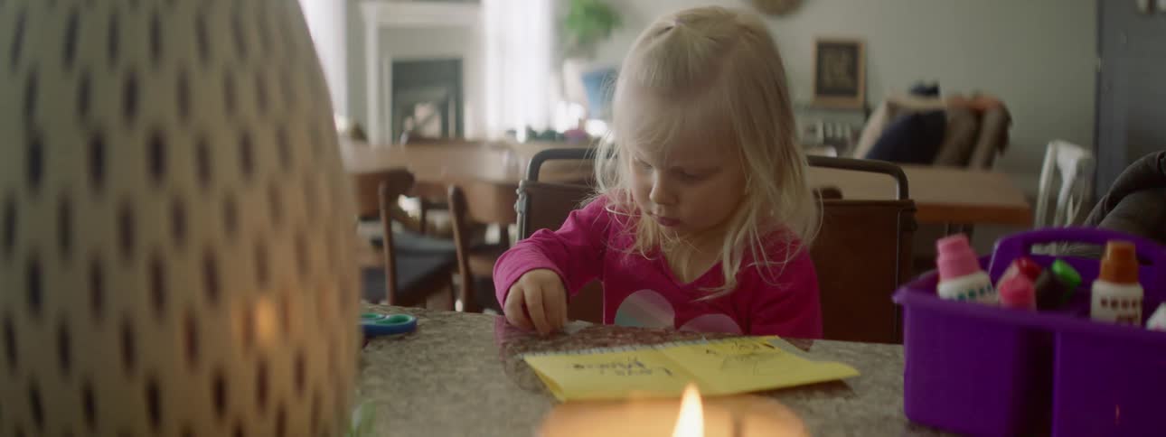 A little girl is doing a project at a table with tape and scissors