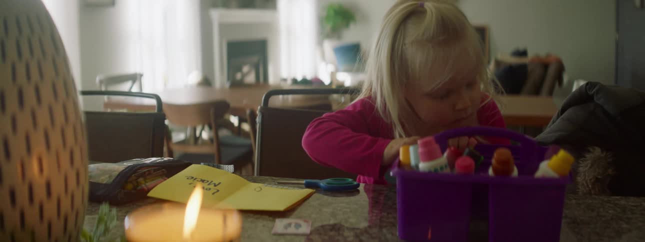 A little girl searching through a bucket for utensils to help her finish making a greeting card
