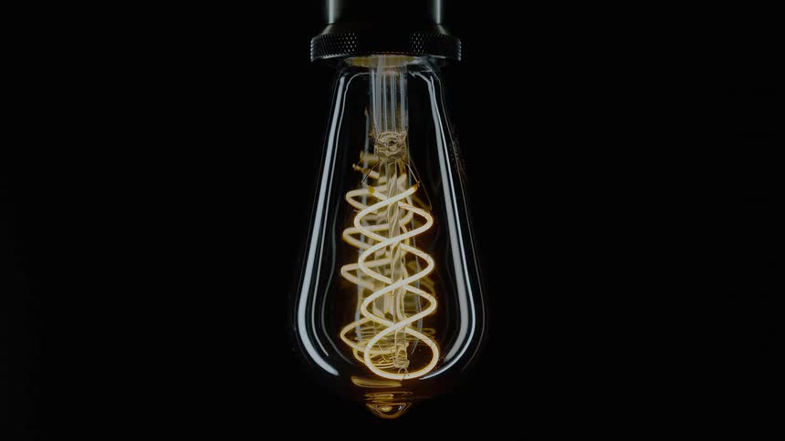 A light bulbs filaments illuminate against a dark background