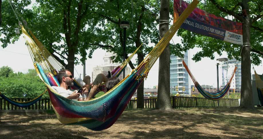 Three people relax in hammocks hanging in a public park