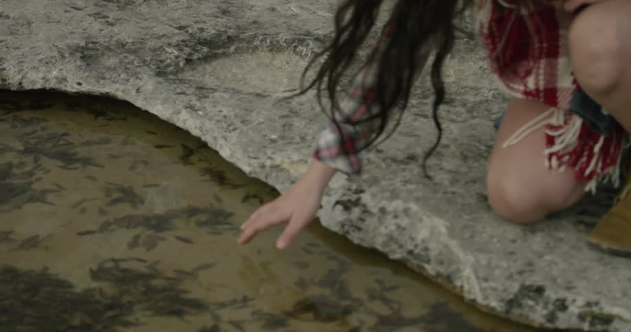A woman kneeling down runs her fingers through a still body of water