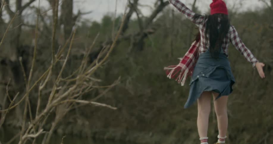 A woman is walking over to some rocks wall waving her arms and climbing down below