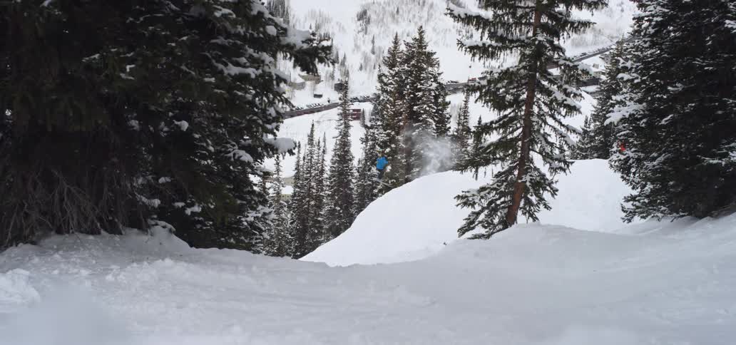 Skier skis up a small slope then jumps and spins and lands on the mountain side