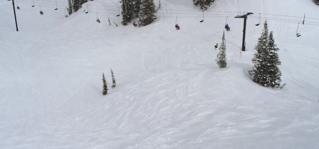 A person skis on a snow covered mountain with ski lifts running above