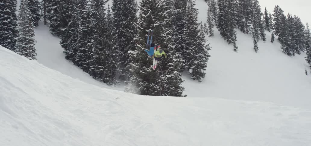 Slow motion of skiers doing a front flip off a jump and landing it