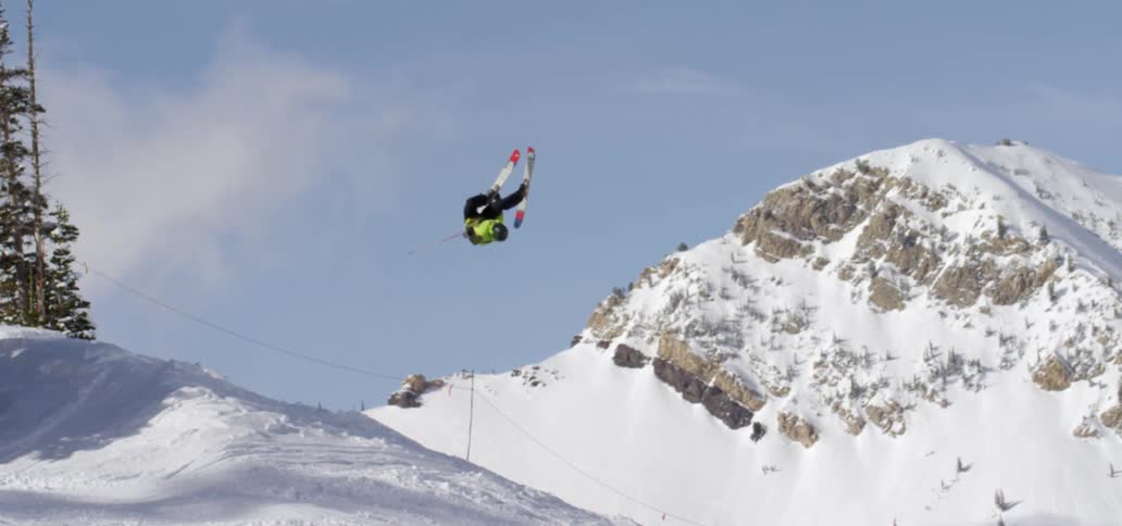 A skier does a back flip off a snow ramp on a mountain slope on a sunny day