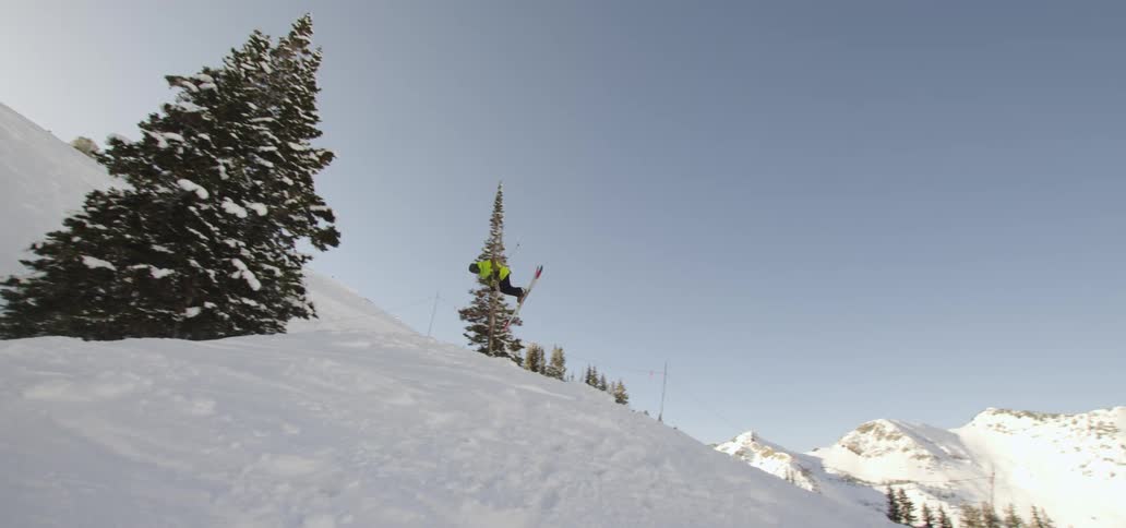 A skier executes a flipping jump over a snow covered hill
