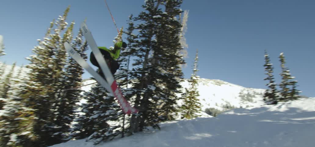 A person skiing and jumping down a snowy slope with trees