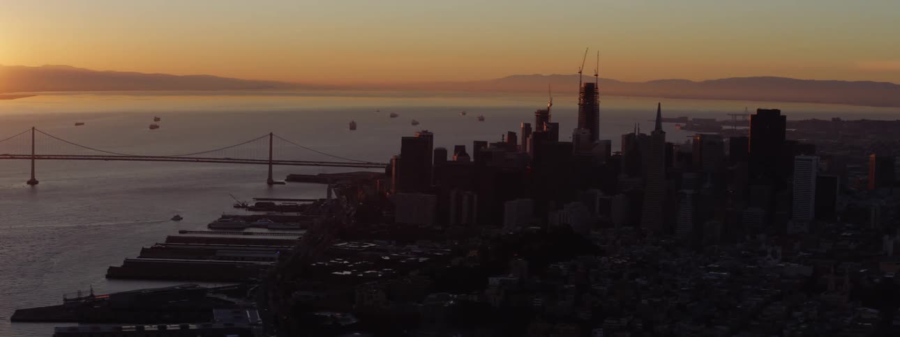 Sun turns hazy horizon orange as watercraft float near bridge and downtown
