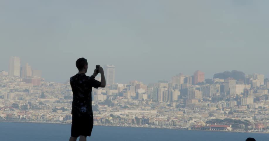 A man takes a picture of the skyline with his cellphone