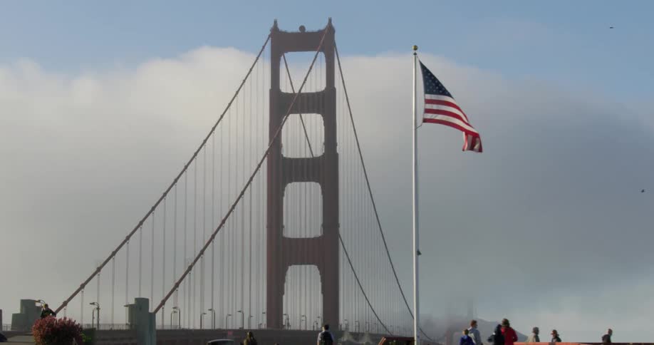 People visit a park next to a suspension bridge