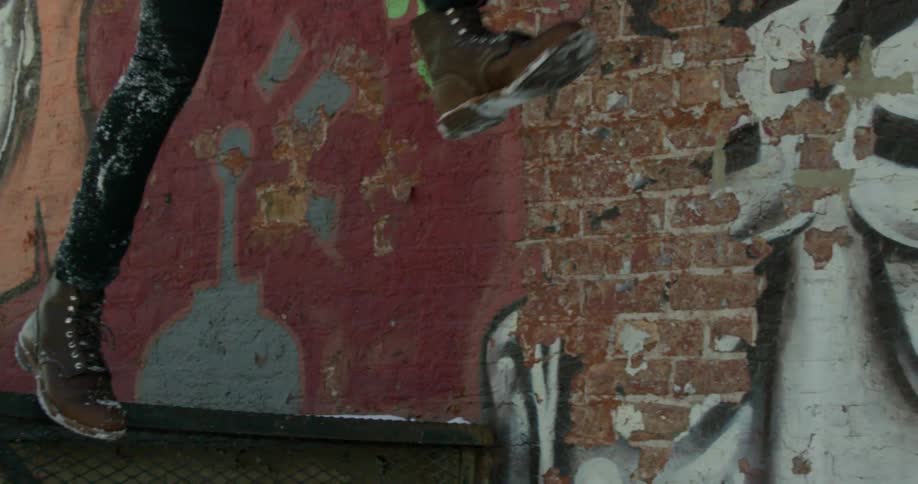 Man runs and jumps in front of a graffitied wall