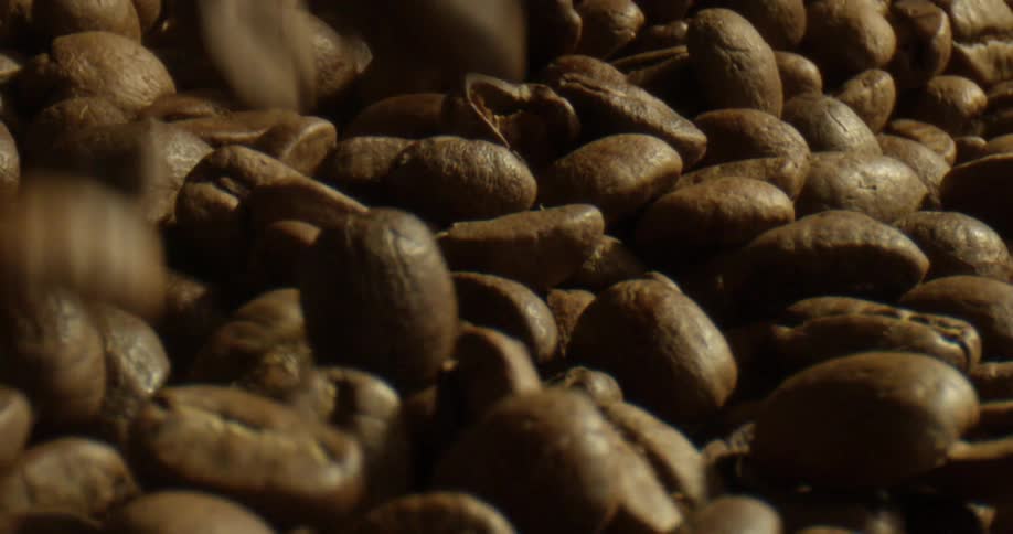 Coffee beans fall and spill over a large pile of other coffee beans