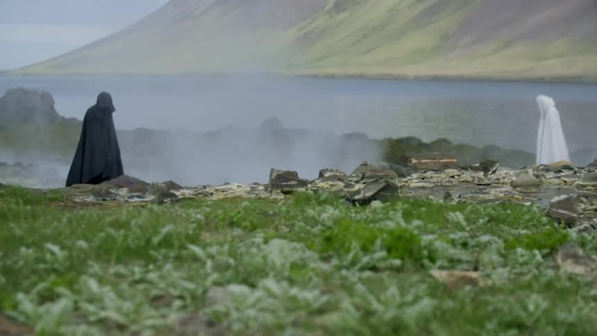 Two cloaked figures on rocky terrain