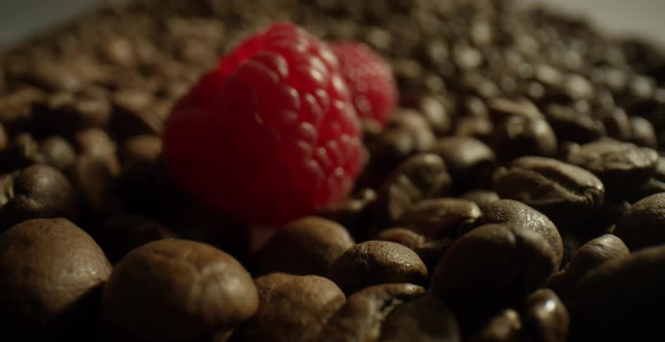 Raspberries are dropped onto a large pile of whole coffee beans
