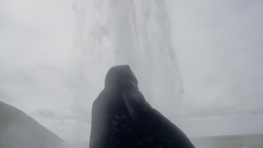 A cloaked figure stands near a waterfall