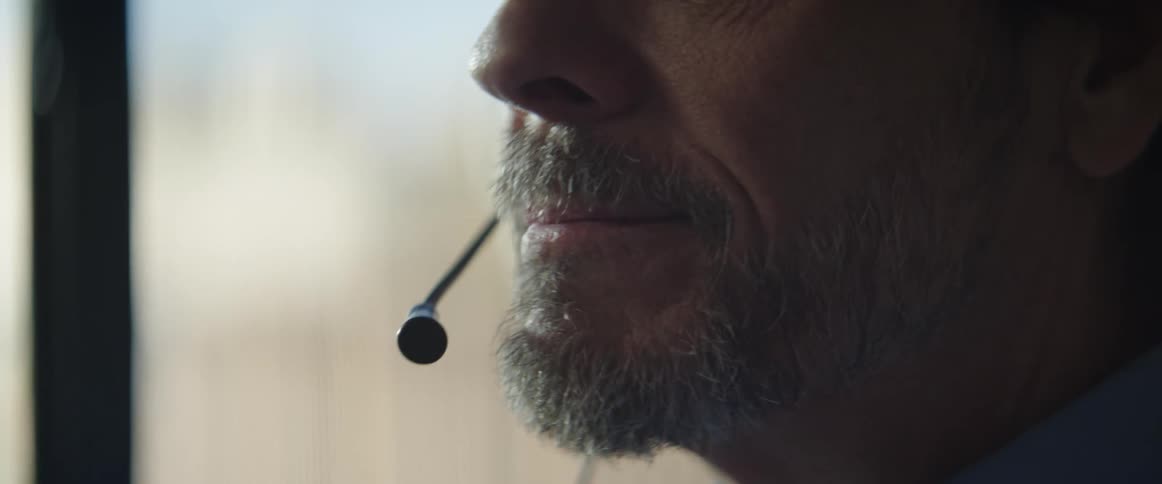 An old man sits in a room and talks on a microphone on a headset