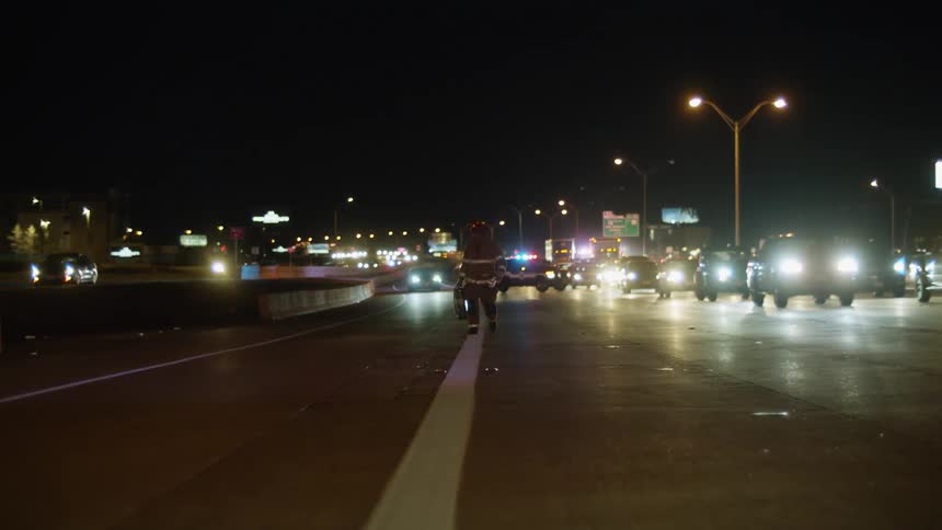 Fireman wearing protective gear walks down the side of the highway away from the fire truck carrying a fire extinguisher