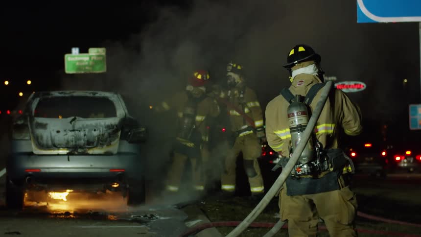 Three firefighters deal with a car fire on a roadway at night