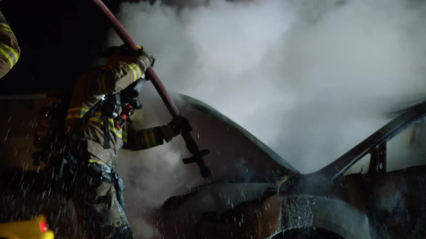 A firefighter sprays a burnt out car engine with water from a hose