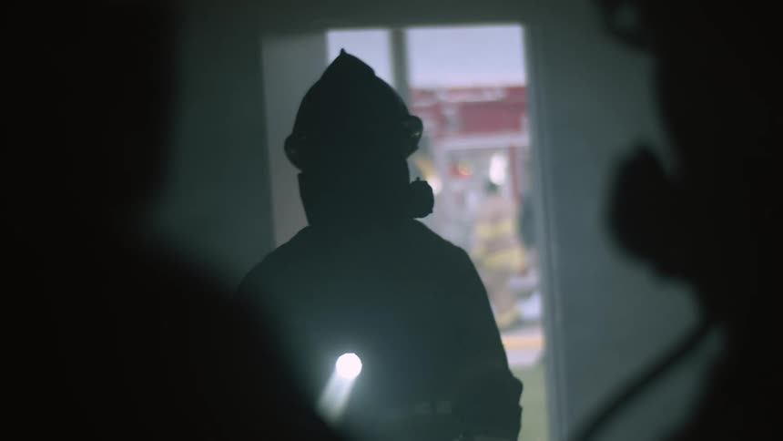 Firefighter shines the flashlight into the dark room