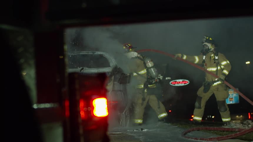 Two firefighters with a hose put out a car fire on a roadway