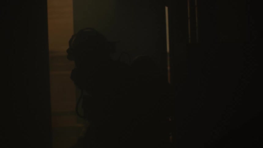 Two firefighters move through a door in a smoky building