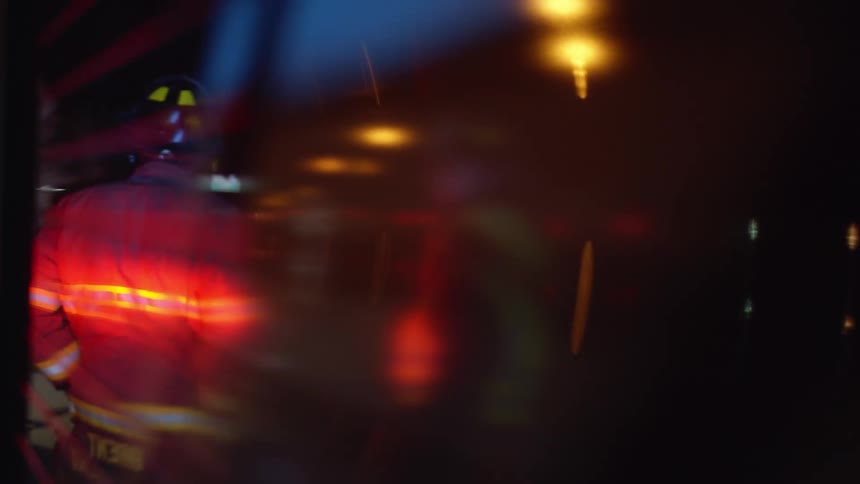 The reflection of firefighters standing near a road at night while sirens flash
