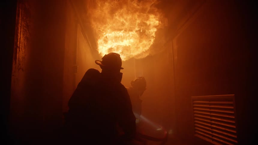 Firefighters in a room with a fire spray water at it
