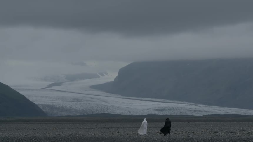 Black and white caped figures stand on rocky ground