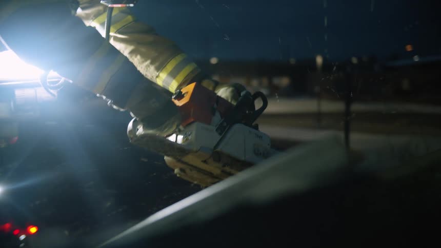 A firefighter uses a chainsaw to cut into the hood of a vehicle