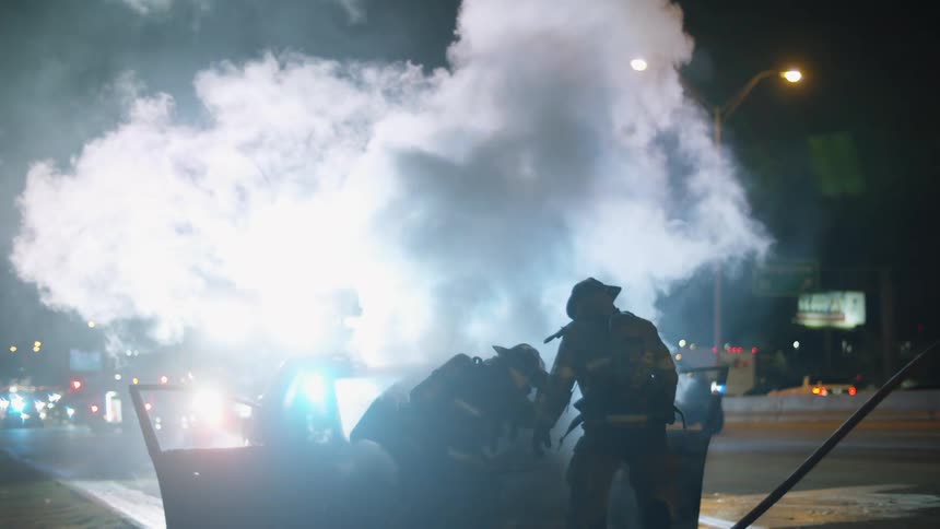 Two firefighters work to put out a car fire on a highway