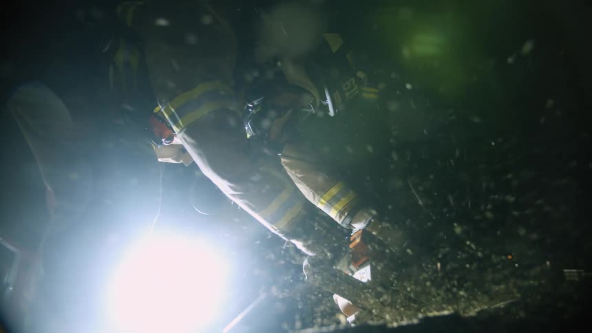A firefighter in helmet and mask uses a saw at night