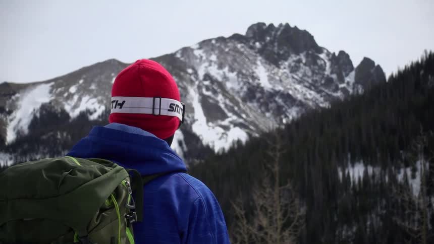 A man with a hat and backpack stands in nature and takes it all in