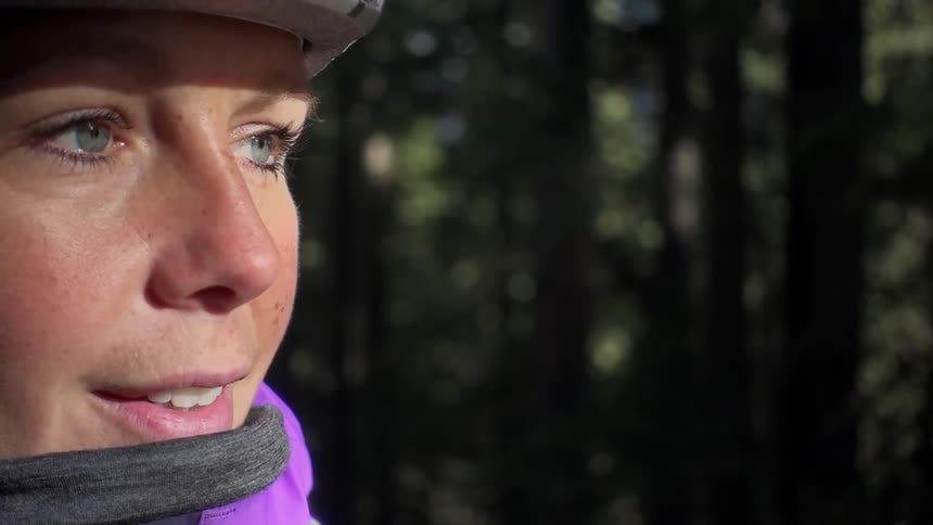 A woman wearing a bike helmet is standing near a forested area