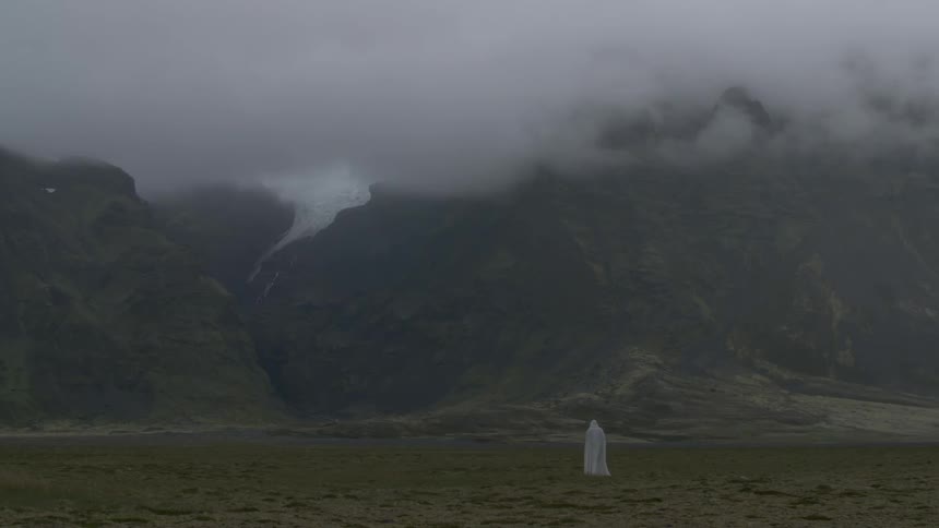 A cloaked figure walks near a mist covered mountain