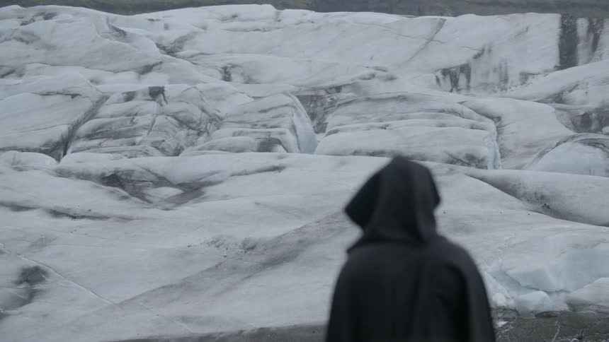 A figure dressed in a long black cape staring at a snow covered shoreline