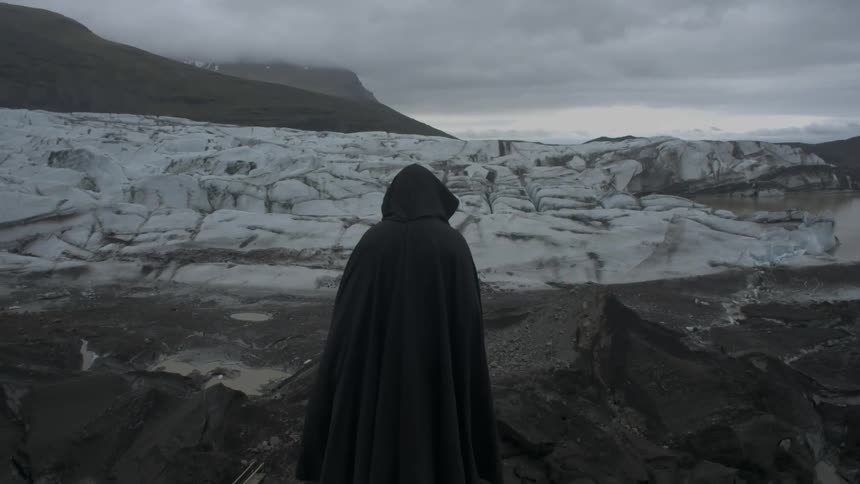A person in a cloak stands near a snowy hill