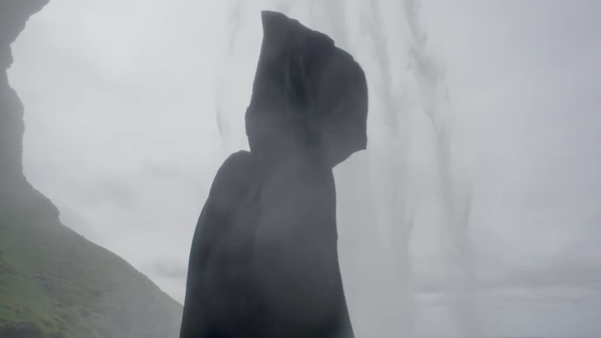 A person wearing dark robes is standing outside on a cloudy day