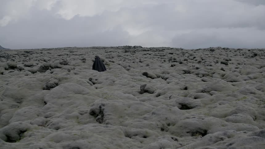 A person wearing black robes is traveling over a field