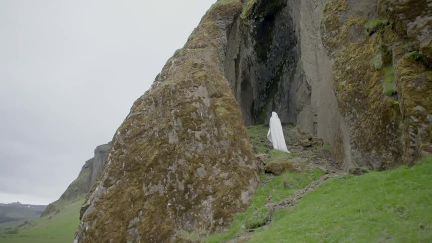 A white-cloaked figure standing between steep, rock walls