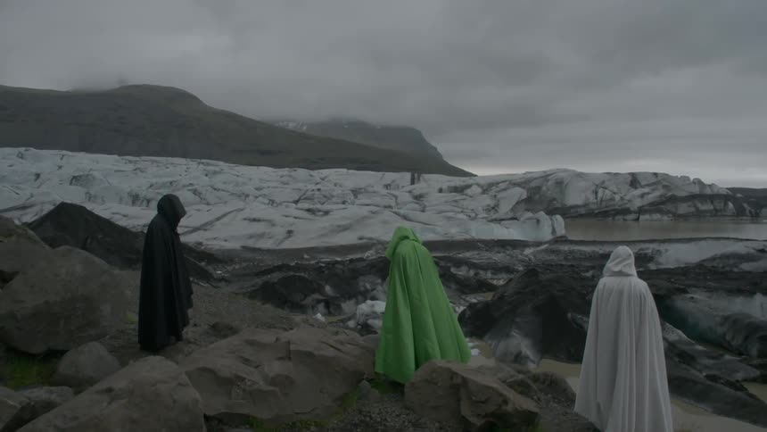 Three people in robes are standing on a hill on a cloudy day